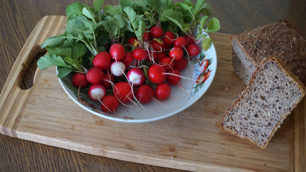A vibrant display of radishes with leafy greens and whole grain bread on a wooden cutting board.